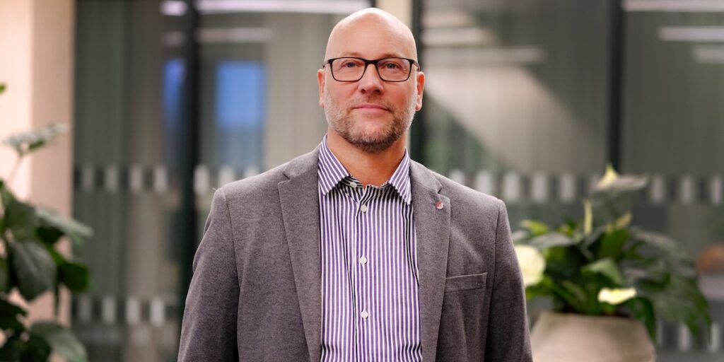 Magnus Lindberg, man i grå kavaj och randigt skjorta med glasögon